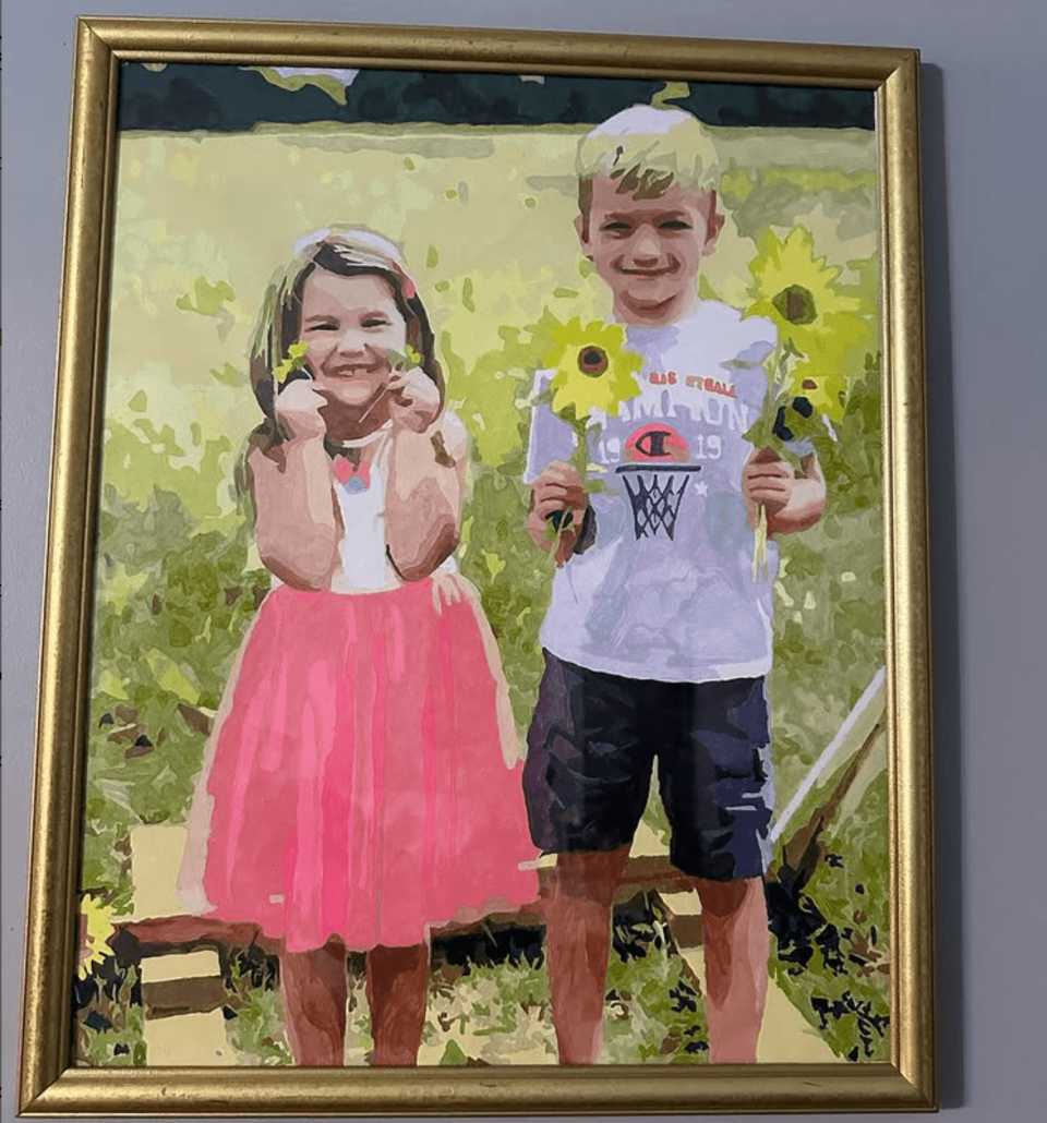 A picture of 2 kids inside a paint by numbers painting hanging on a wall.
