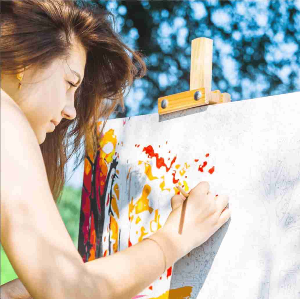A lady painting her paint by numbers canvas in a field.