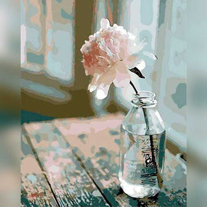 Clear glass bottle with a single pink flower on a wooden surface with abstract patterns.