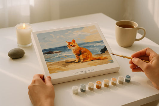 A paint by numbers painting of a orange cat, a hand slowly drawing it with a brush in a hand and paints pot kept in a white clean table.