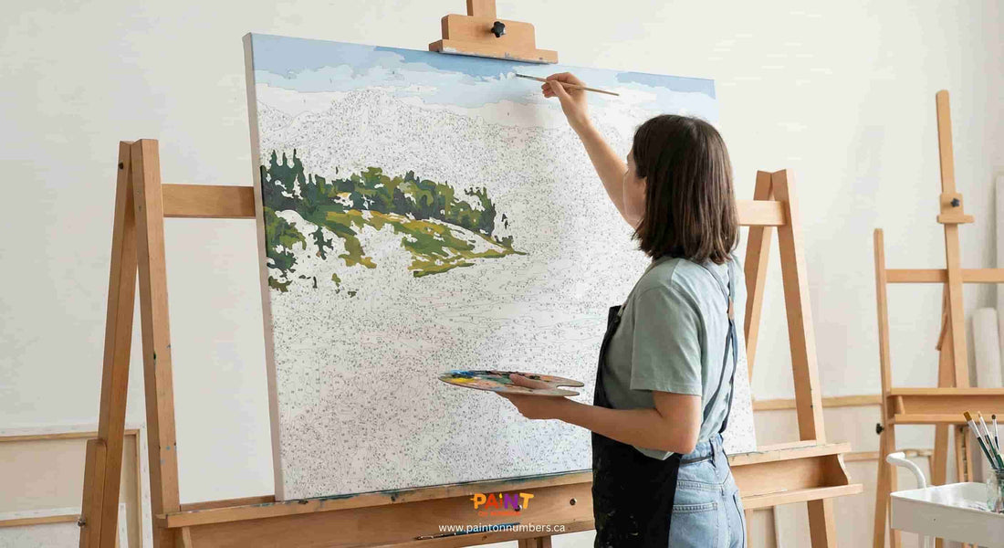 An artist working on a large paint by numbers canvas using an easel for support.