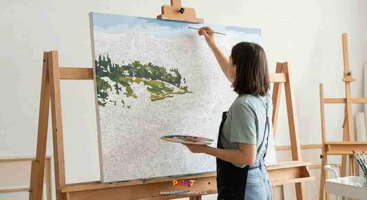 An artist working on a large paint by numbers canvas using an easel for support.