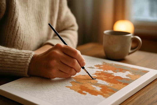 Close-up of a person’s hand painting a paint by numbers canvas with warm colors, a mug of coffee beside them, creating a cozy and mindful winter atmosphere