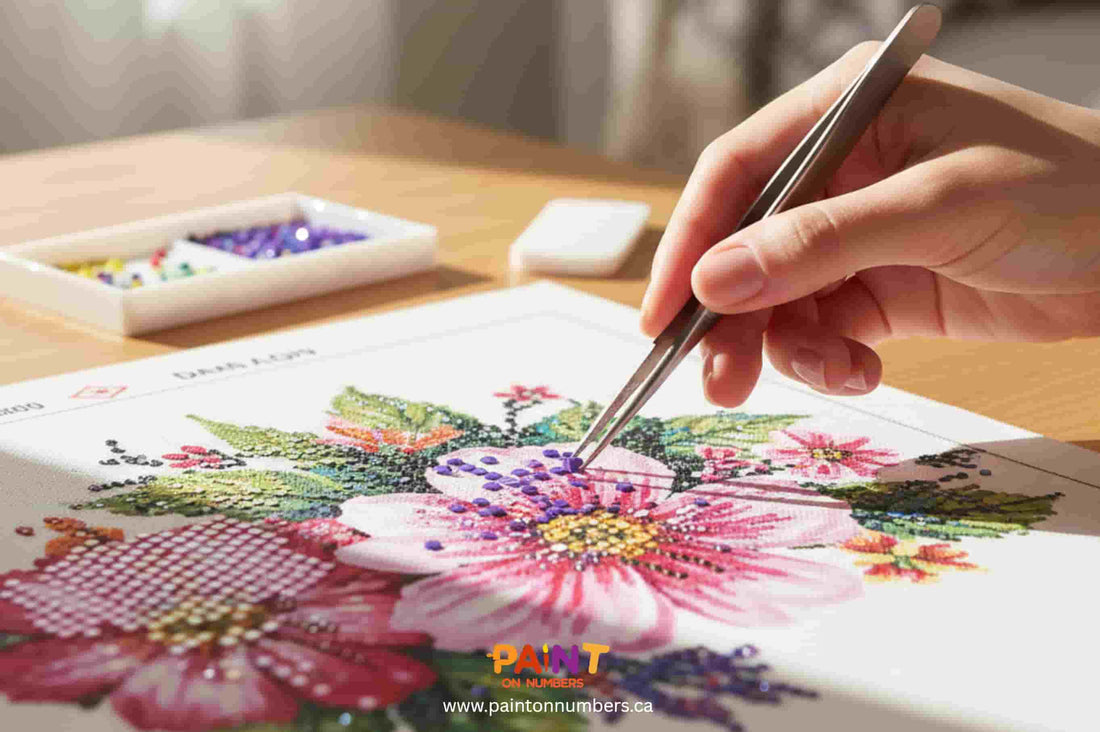 Hand using tweezers to fix misplaced drills on a floral diamond painting canvas, with colorful beads and tools on a wooden table — Paint On Numbers Canada.