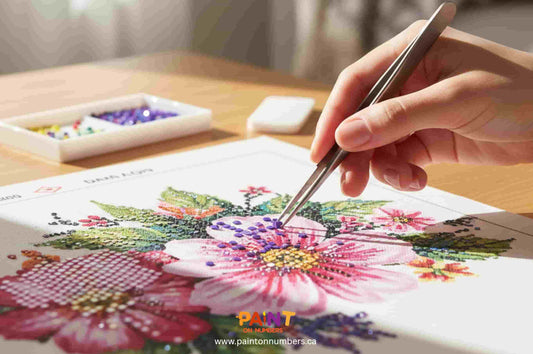 Hand using tweezers to fix misplaced drills on a floral diamond painting canvas, with colorful beads and tools on a wooden table — Paint On Numbers Canada.
