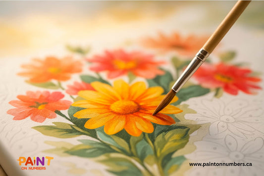 Close-up of a paint by numbers floral canvas being painted, with a brush coloring a bright orange-yellow flower while unpainted outlines remain visible.