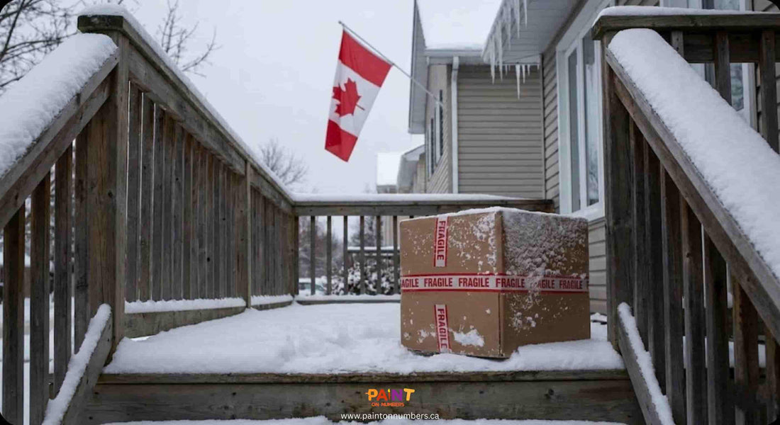 A cardboard shipping box marked FRAGILE covered in fresh snow, sitting on a frozen wooden porch with a Canadian flag in the background, illustrating winter paint by numbers delivery conditions.