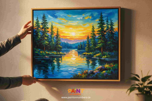 Hands hanging a vibrant landscape paint by numbers painting with a lake and forest scene in a cozy living room.