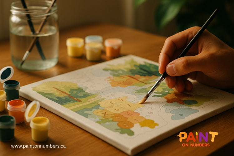 A wooden desk showing a paint by numbers painting and a hand drawing the painting.