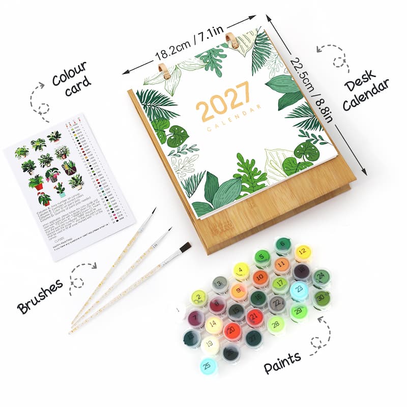 A desk calendar painting kit shown on a white background with labeled callouts for the desk calendar, colour card, brushes, and paints. The calendar has a bamboo wood base and a white cover decorated with green tropical leaves and the year 2027.