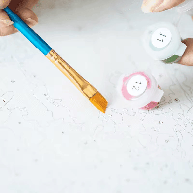 Close-up of Paint By Numbers Kit showing a flat paintbrush, numbered paint pots, and a detailed canvas with outlines