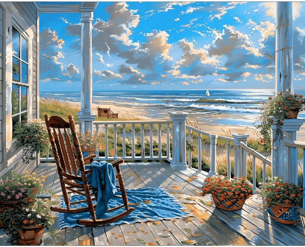 "Sunset by Seaside Paint By Numbers painting showcasing a cozy front porch with a wooden rocking chair, blue blanket, potted flowers, and ocean waves under a golden evening sky."