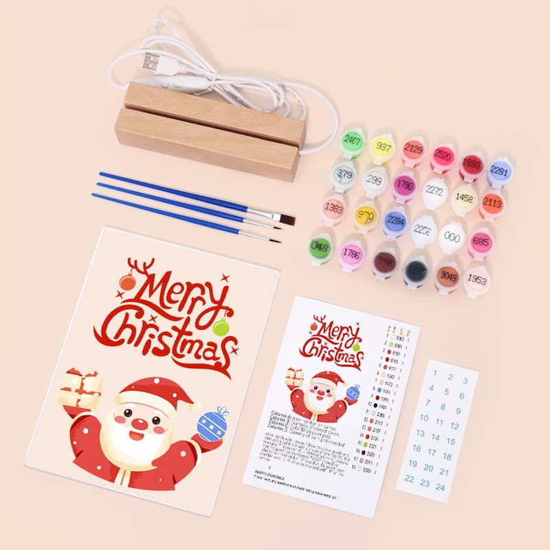 Christmas-themed DIY canvas painting kit laid out on a light beige background, including a wooden block, USB charging cable, paintbrushes, multiple small colorful paint pots, a Santa illustration card, a color reference sheet, and a numbered sticker sheet.