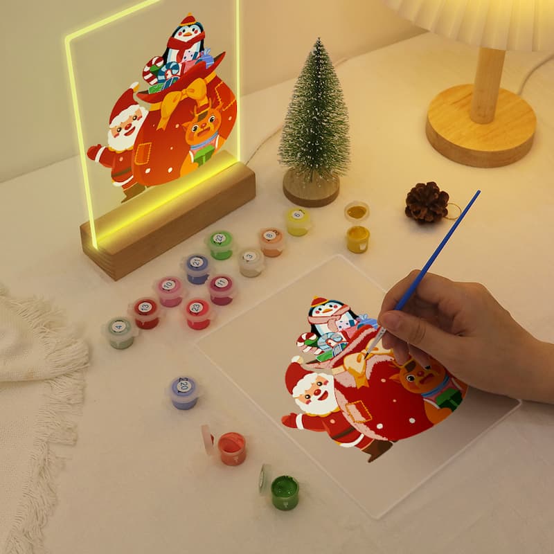 Neon sign of Santa Claus and reindeer with a hand painting a similar design on paper.