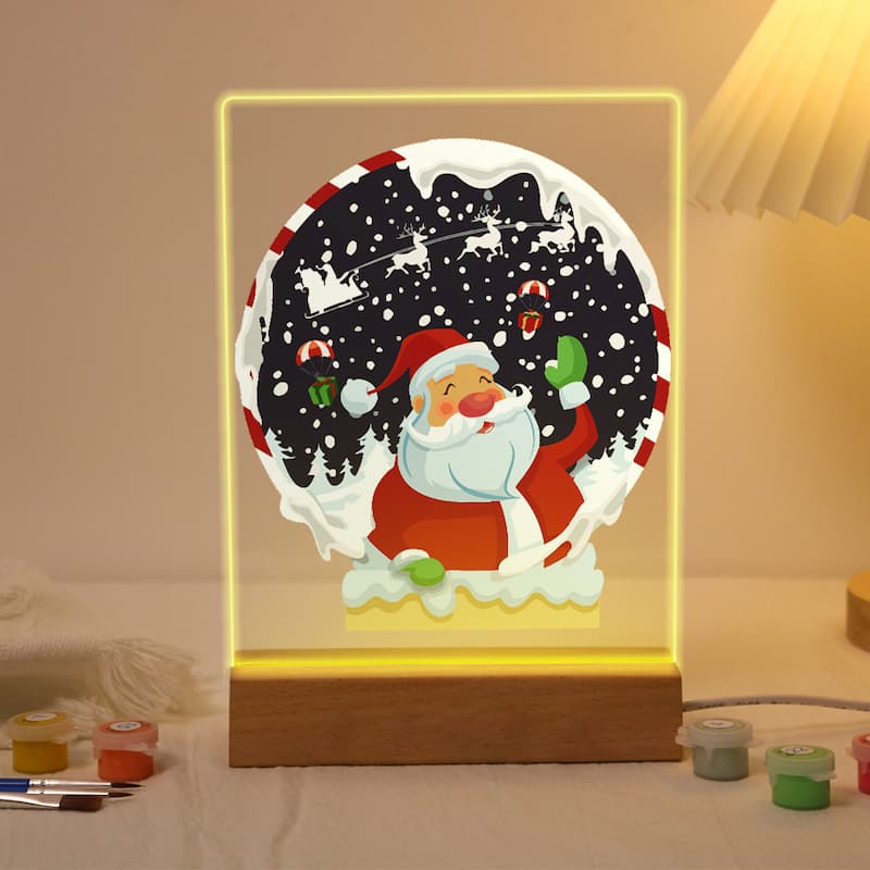 A glowing acrylic LED light box featuring a festive Christmas scene with Santa Claus inside a snowy globe design, set on a wooden base on a tabletop.