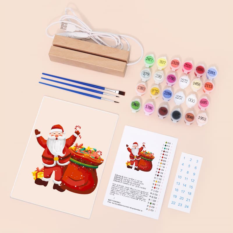 Christmas-themed painting kit with Santa Claus illustration, paint bottles, brushes, and a USB cable on a beige background.