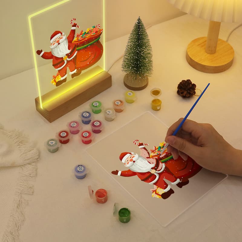 Hand painting a 3D Santa Claus figure on a clear acrylic sheet with a neon sign of Santa Claus in the background.