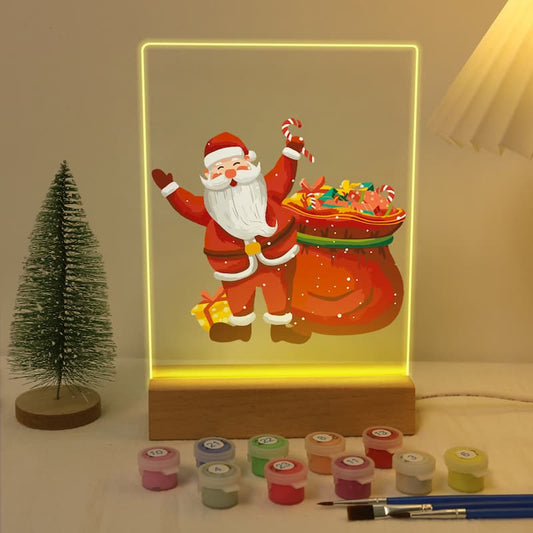 Decorative light box with Santa Claus design, surrounded by small containers and a brush on a neutral background.