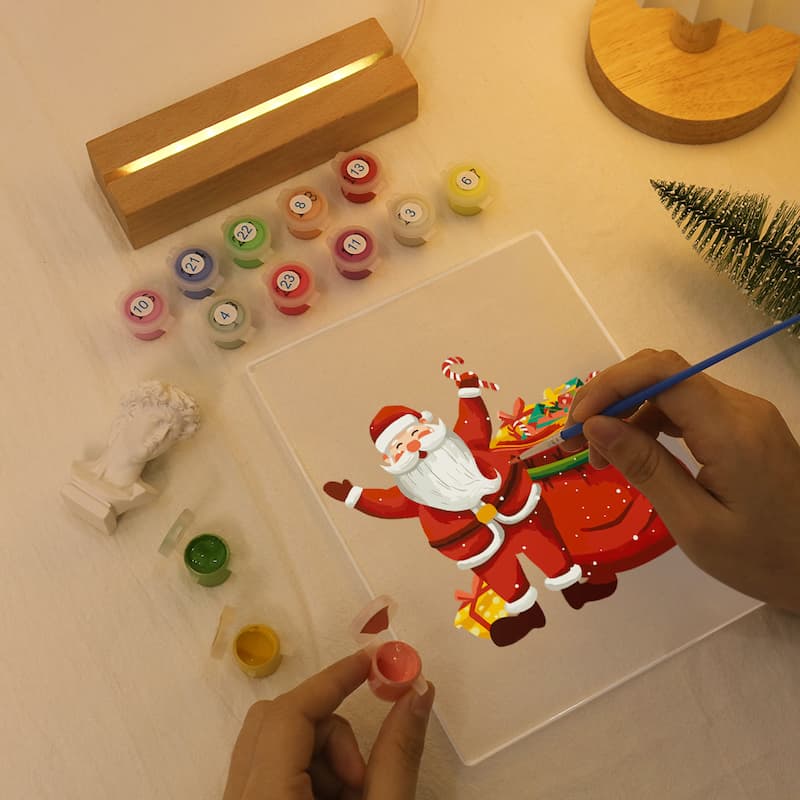 Person painting a cartoon Santa Claus on a clear acrylic block with various colors and tools.