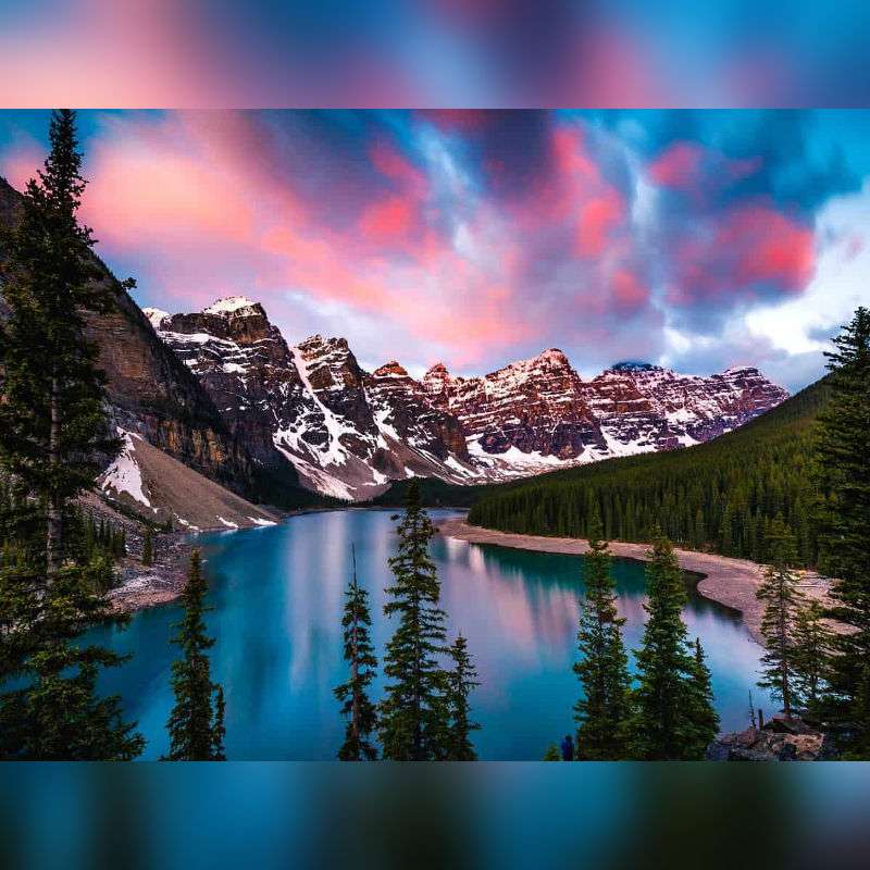 Sunrise at Lake Moraine Paint By Numbers painting featuring vibrant pink and blue sky over snow-covered Rocky Mountains, turquoise lake, and lush pine forest in Alberta, Canada.