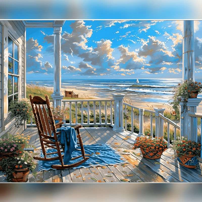 Sunset by Seaside Paint By Numbers painting showcasing a cozy front porch with a wooden rocking chair, blue blanket, potted flowers, and ocean waves under a golden evening sky.