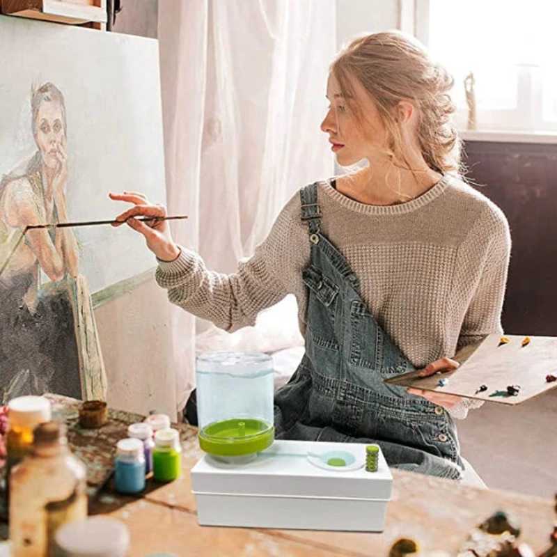 Woman artist using Automatic Brush Cleaner while painting in studio with canvas and palette