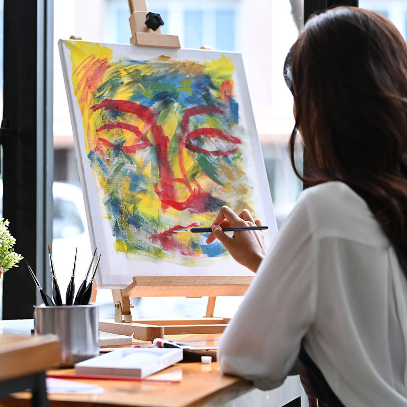 Person painting a colorful abstract face on an easel