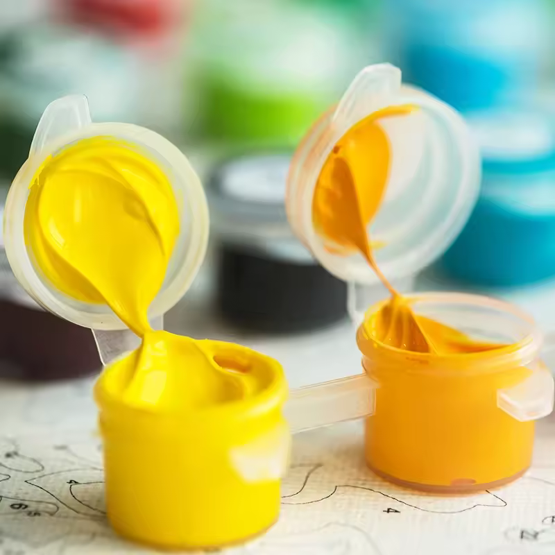 Yellow and orange paint pots from a Paint By Numbers Kit Canada placed on top of a numbered canvas with vibrant background colors
