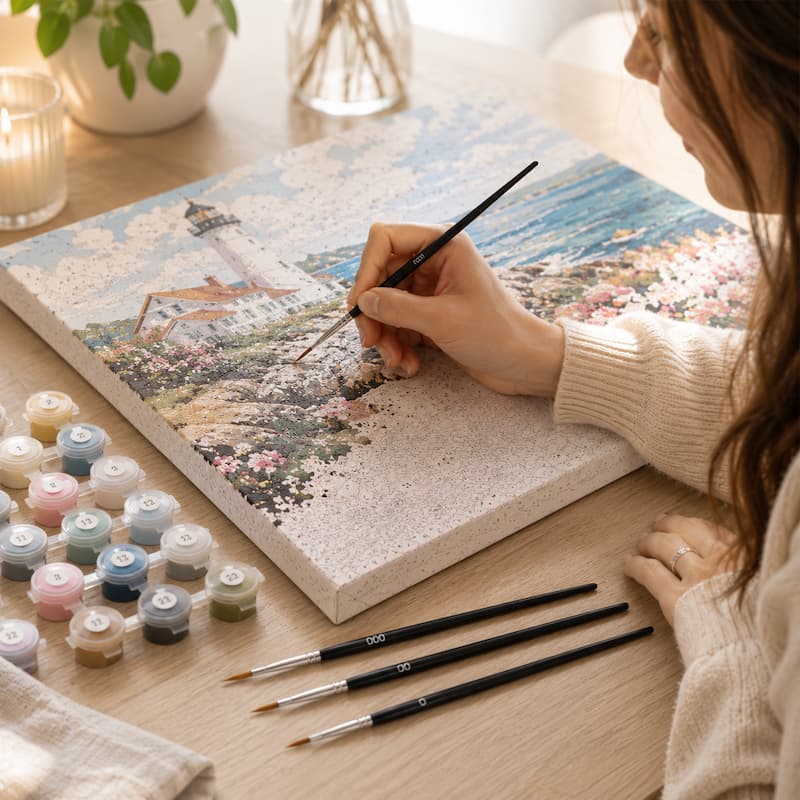 Person painting a scenic landscape on a canvas with art supplies on a table.