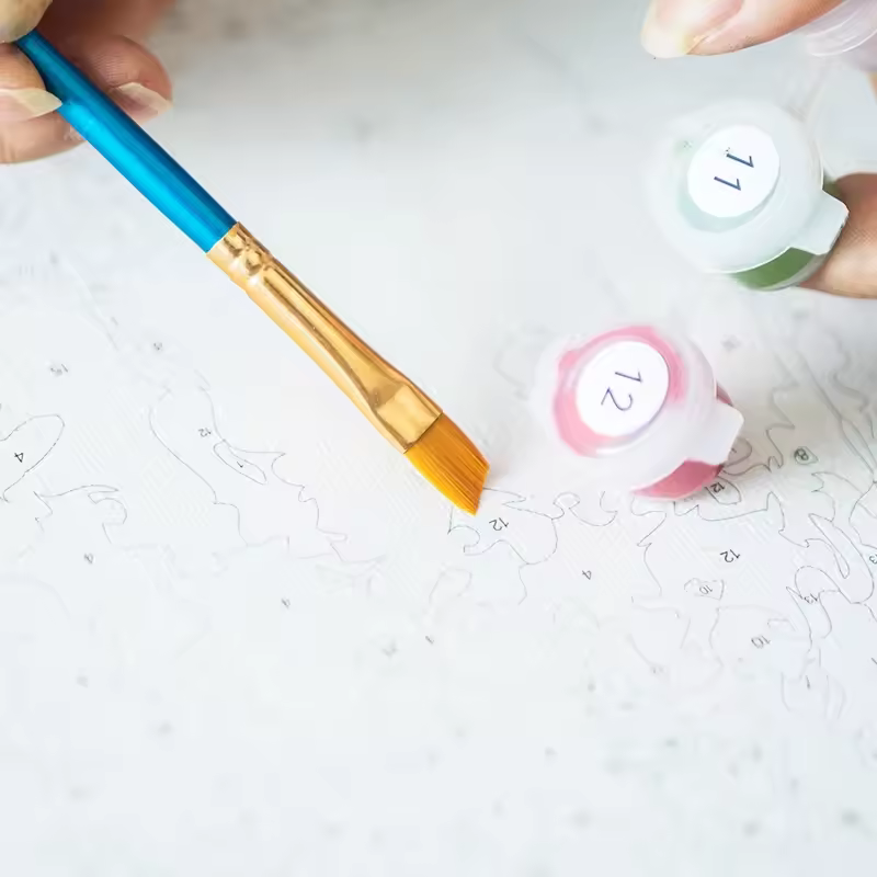 Close-up of Paint By Numbers Kit Canada showing a flat paintbrush, numbered paint pots, and a detailed canvas with outlines