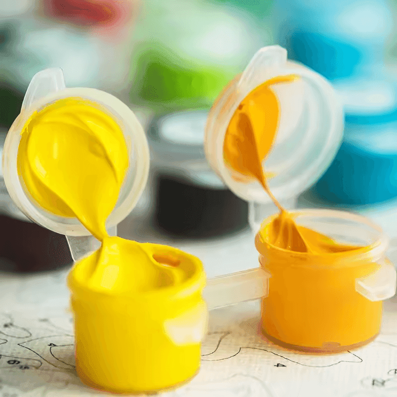 Yellow and orange paint pots from a Paint By Numbers Kit Canada placed on top of a numbered canvas with vibrant background colors